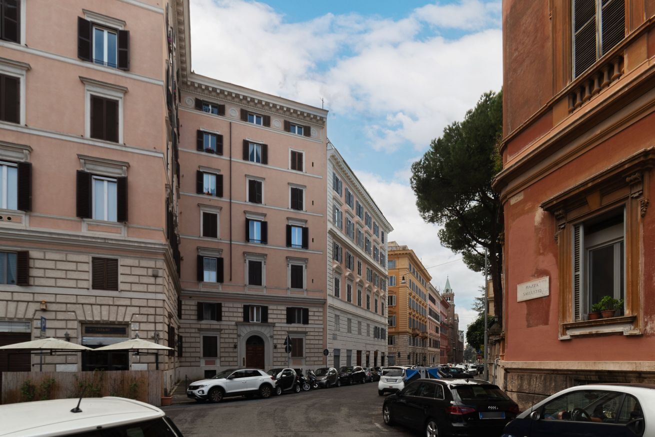 A street view with parked cars, multi-story buildings, and a clear sky.