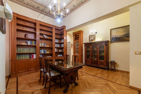 A library with wooden bookshelves, a glass-top table, and chairs.