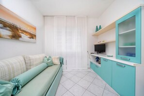 A compact living space with a sofa, a TV, teal cabinets, and a painting on the wall.