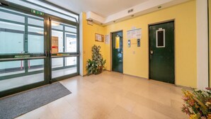 Eine Lobby mit Glastür, grüner Tür, einer Pflanze und einer gelben Wand.