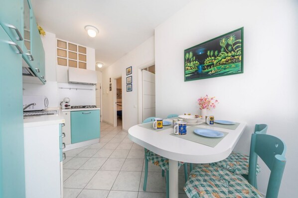A kitchen with teal cabinets, a white countertop, and a dining area with a white table and chairs.