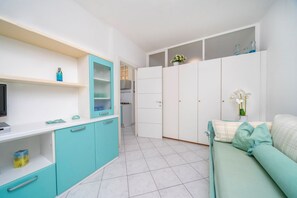 A compact living space with a kitchenette, a sofa, and a TV. - GuestHost - Raggio dello Scirocco Apartment - Lignano Pineta (Lignano Sabbiadoro)