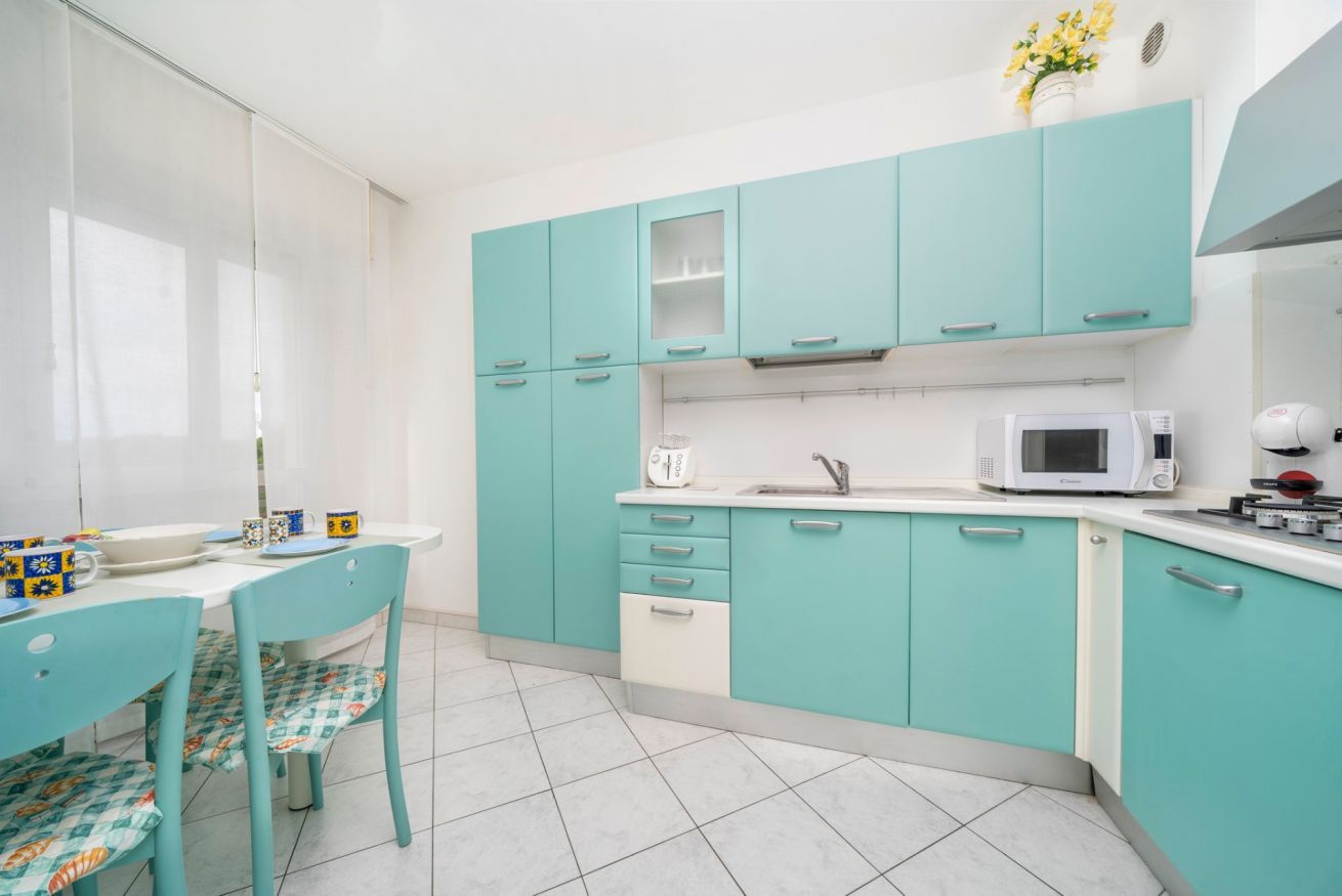 A kitchen with teal cabinets, a white countertop, a microwave, and a coffee maker.
