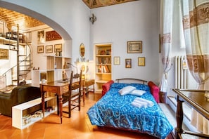 Een slaapkamer met een bed, een bureau, een stoel, een boekenkast en een spiraaltrap.