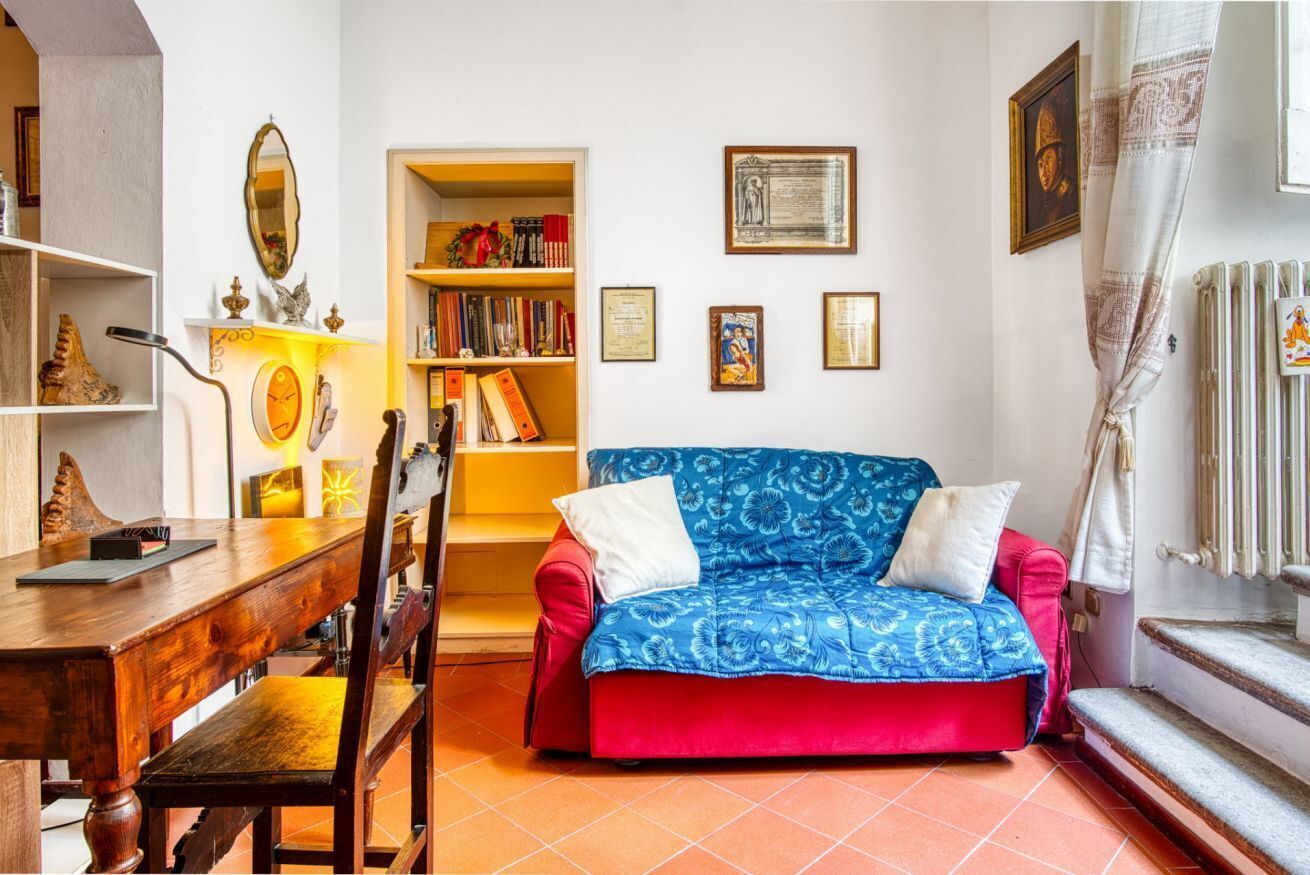 Ein gemütliches Wohnzimmer mit einem Holztisch, einem rot-blauen Sofa, einem Bücherregal und einer Heizung.