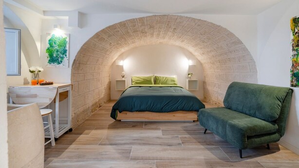A bedroom with a stone arch, a bed with green bedding, a green sofa, and a desk with a chair. - GuestHost - Charming and quiet 30 sqm room in the heart of Bari, perfect for two people. Located on the first floor of an elegant building (access via stairs), the room is furnished with taste and attention to detail, creating a welcoming and charming at (Bari)