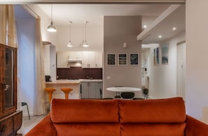 A modern living room with a sofa, a dining area with a table and chairs, a kitchen with cabinets and a sink, and a hallway with artwork on the walls.