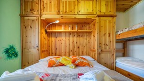Een houten kamer in chaletstijl met een stapelbed, een bed met bloemenkussens en een lamp.