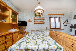 Une chambre à coucher avec un lit en bois, un bureau, une télévision, une fenêtre avec des rideaux et une étagère ornée d’objets décoratifs.
