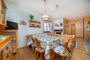 Een eethoek met een houten tafel en stoelen, een televisie en een keuken op de achtergrond.