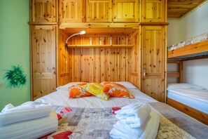 A wooden cabin-style room with a bunk bed, a bed with floral pillows, and a lamp. - GuestHost - Casa Margherita - Valbruna  (Valbruna)