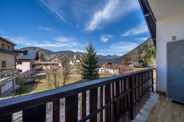 A balcony with a view of a mountainous landscape, a wooden railing, and a building with a sloped roof.