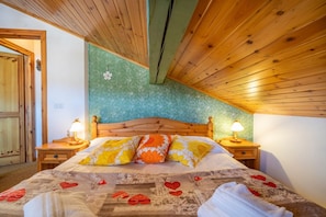 Een slaapkamer met een houten plafond, een bed met beddengoed met een patroon, twee bedlampen en een groene, gestructureerde wand.
