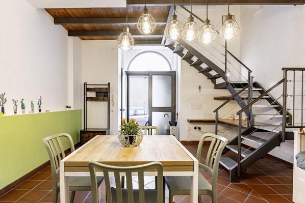 A dining area with a wooden table and chairs, a staircase, and pendant lights.