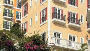 Un edificio de varios pisos con balcones, una escalera de piedra adornada con flores rosadas y un cartel indicador.