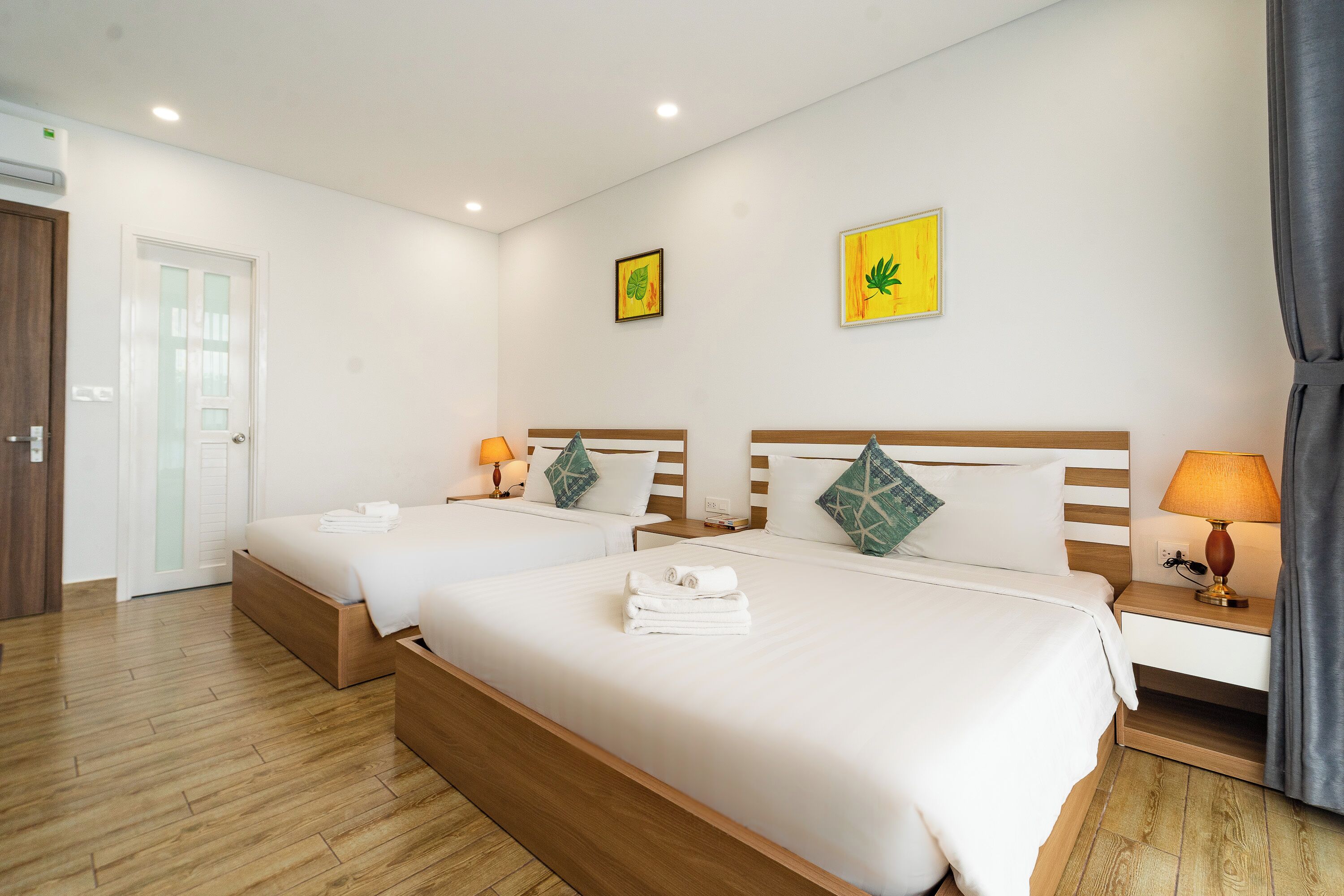 Habitación de hotel con dos camas, cabeceros de madera, ropa de cama blanca y dos lámparas fijadas a la pared.