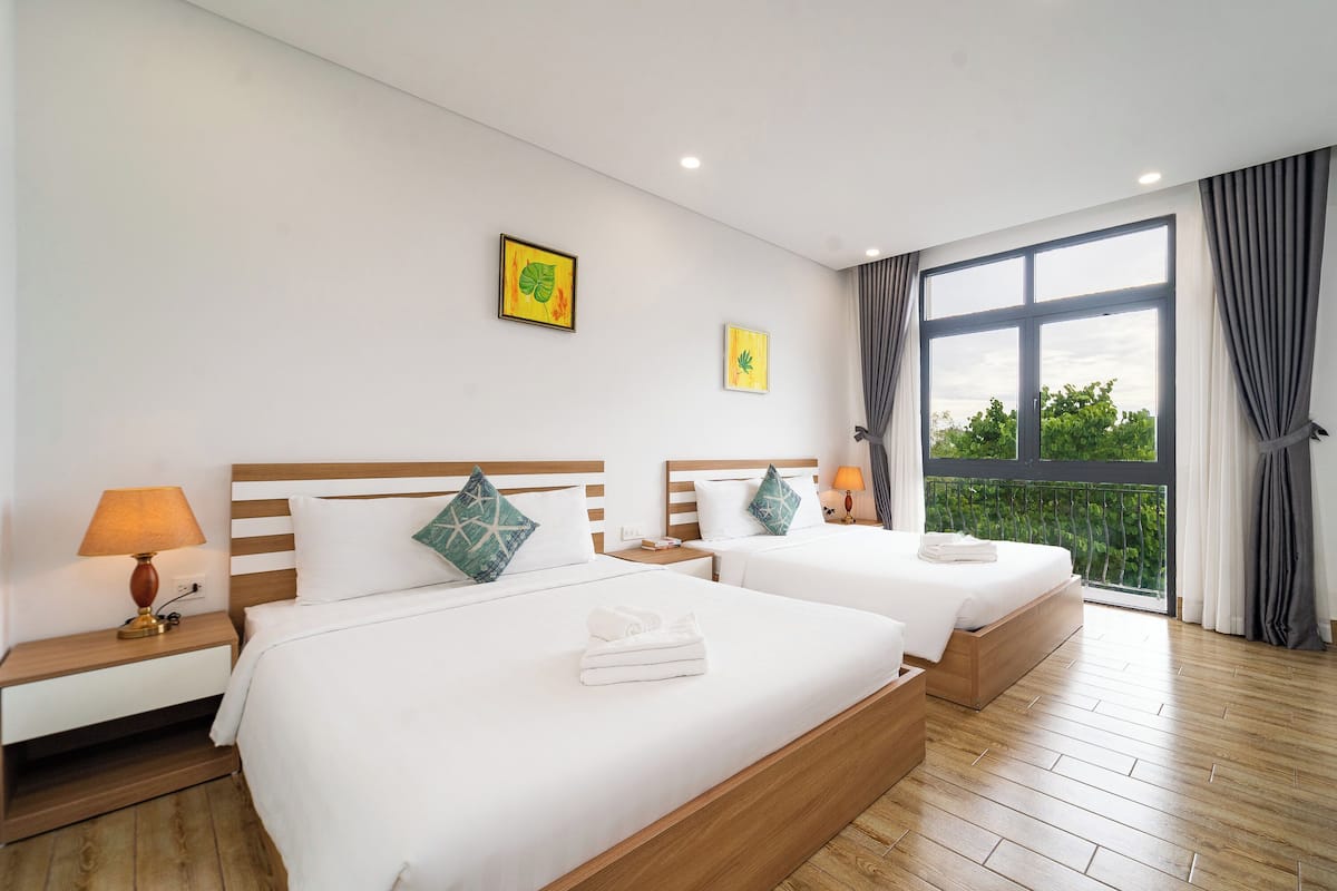 Een hotelkamer met twee bedden, houten vloeren, een groot raam met gordijnen en kunstwerken aan de muur.