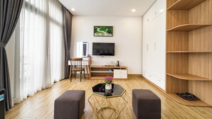 Una sala de estar moderna con piso de madera, una mesa de centro negra con un florero, un televisor montado en la pared, un escritorio con una silla y estanterías empotradas de madera.