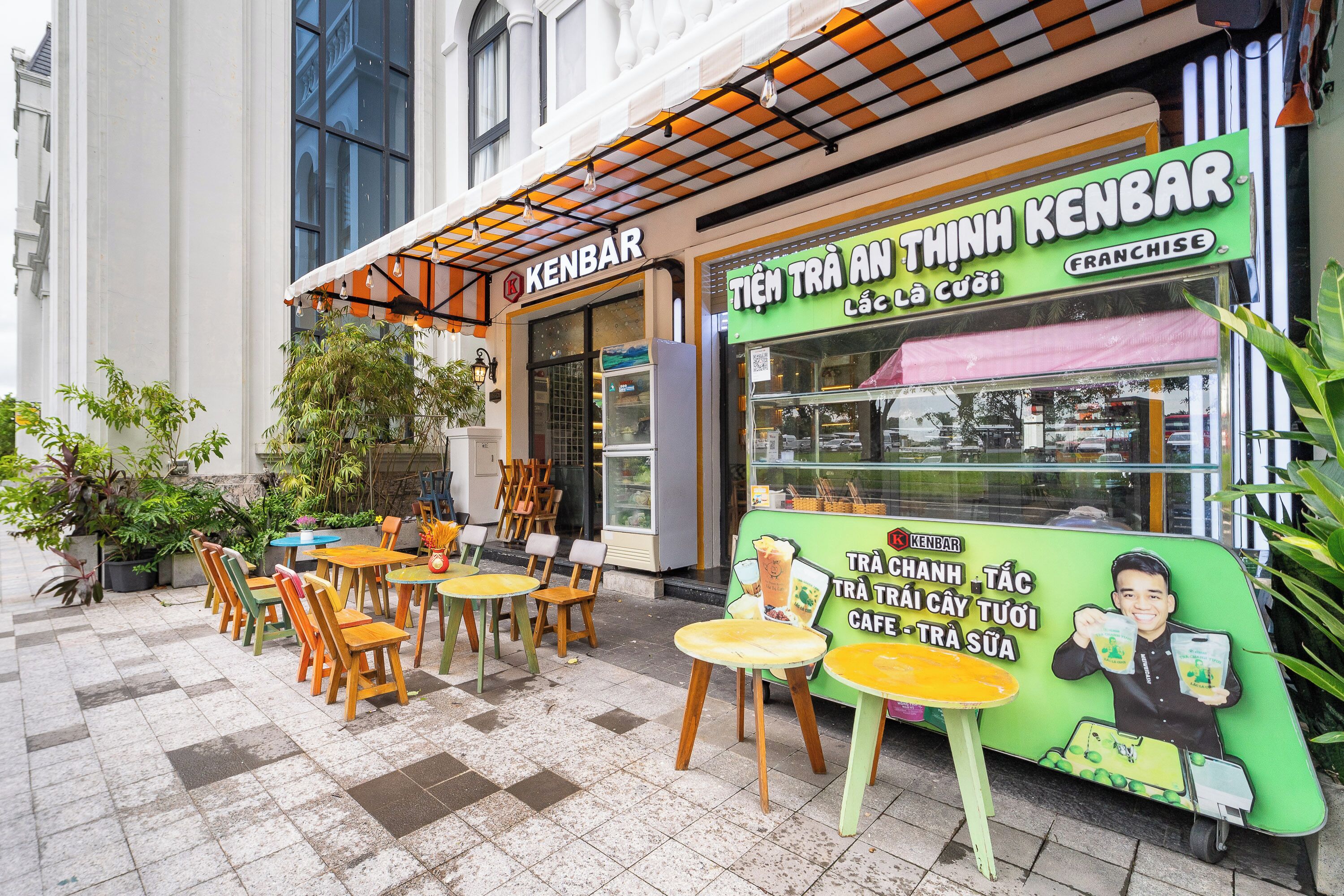 Een café met terras en een groen luifel waarop de naam 'KENBAR' staat.
