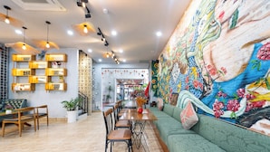 Un comedor con una mesa larga, sillas y un sofá verde. Hay un mural colorido en la pared y un adorno mural estampado.