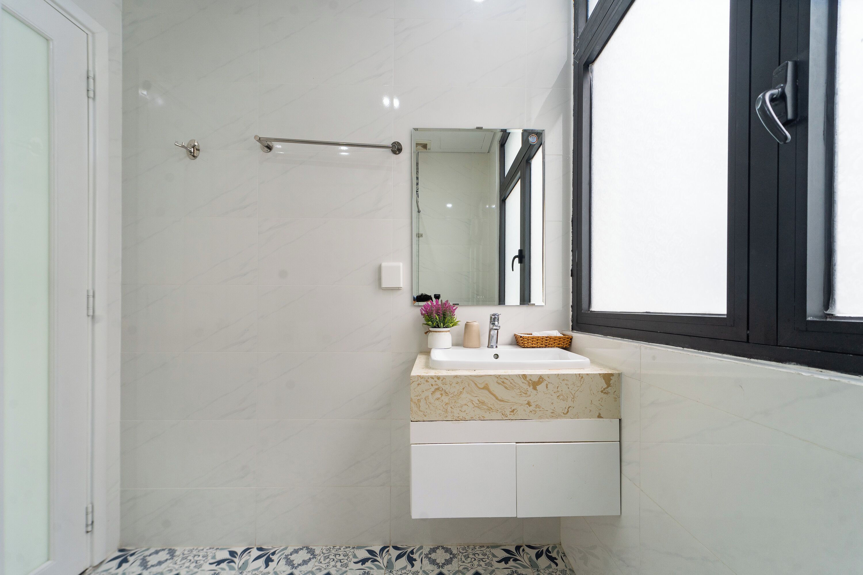 Une salle de bain avec un lavabo en marbre blanc, un miroir et une fenêtre à cadre noir.