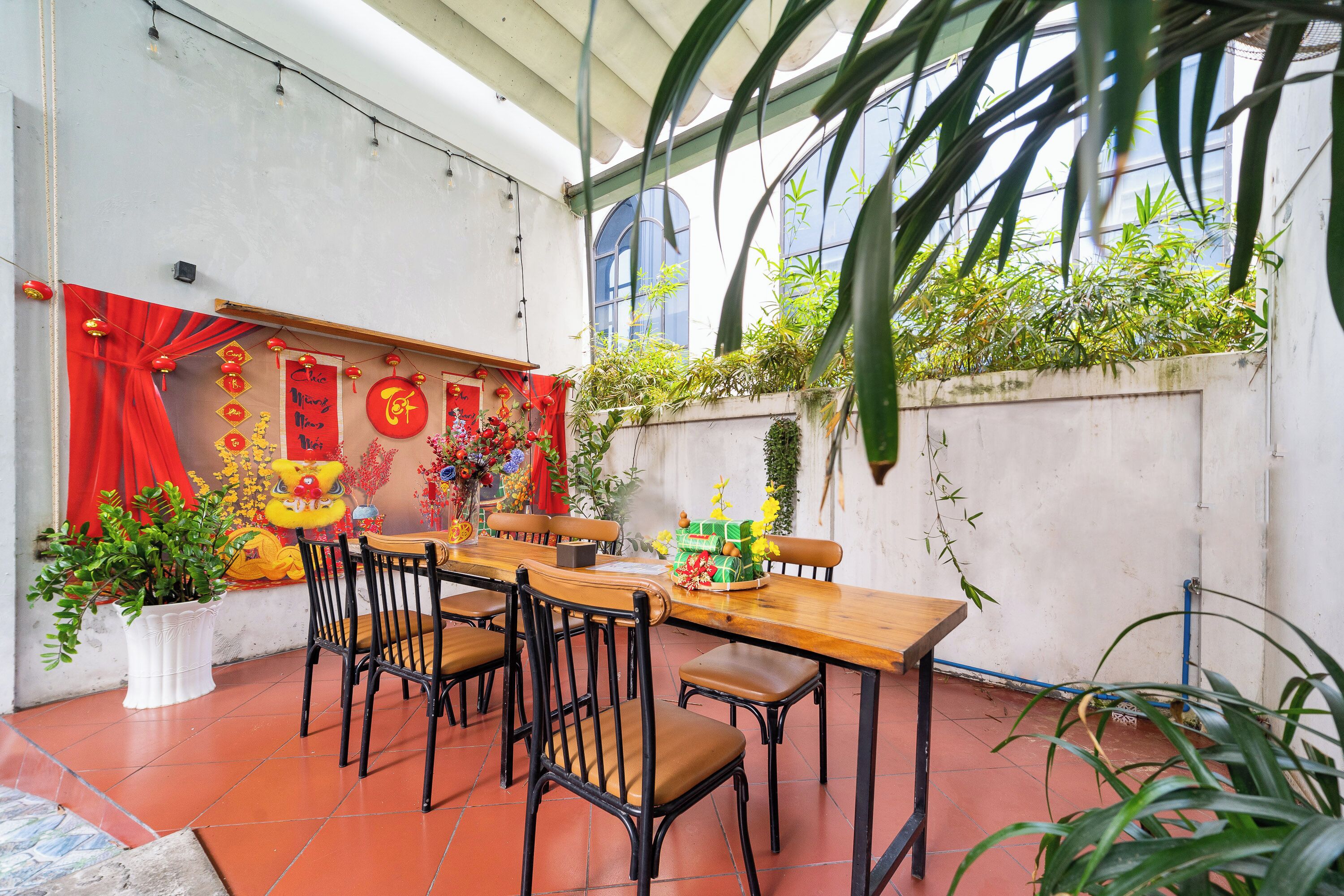 A dining area with a wooden table and chairs, red decorations, and potted plants.