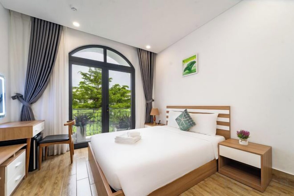 A hotel room with a bed, bedside table, desk, chair, and a window with curtains.