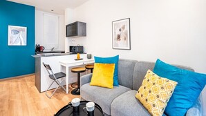 A compact living space with a kitchenette, a grey sofa with colorful cushions, a small dining table, and a foldable chair. - GuestHost - Old Bridge Lovely Apartment (Firenze)