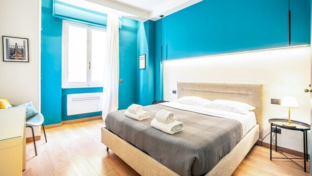 A hotel room with a bed, a desk, a chair, a window with curtains, and a wall with a picture. - GuestHost - Old Bridge Lovely Apartment (Firenze)