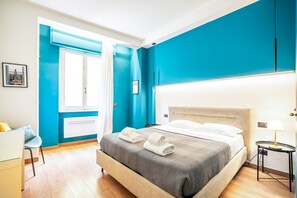 A hotel room with a bed, a desk, a chair, a window with curtains, and a wall with a picture.