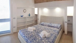 Une chambre avec un lit, des étagères intégrées, une fenêtre avec des stores et un plafond en briques.