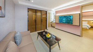 Habitació d'hotel moderna amb un sofà, una taula de vidre amb fruita, una televisió i un armari amb portes corredisses.