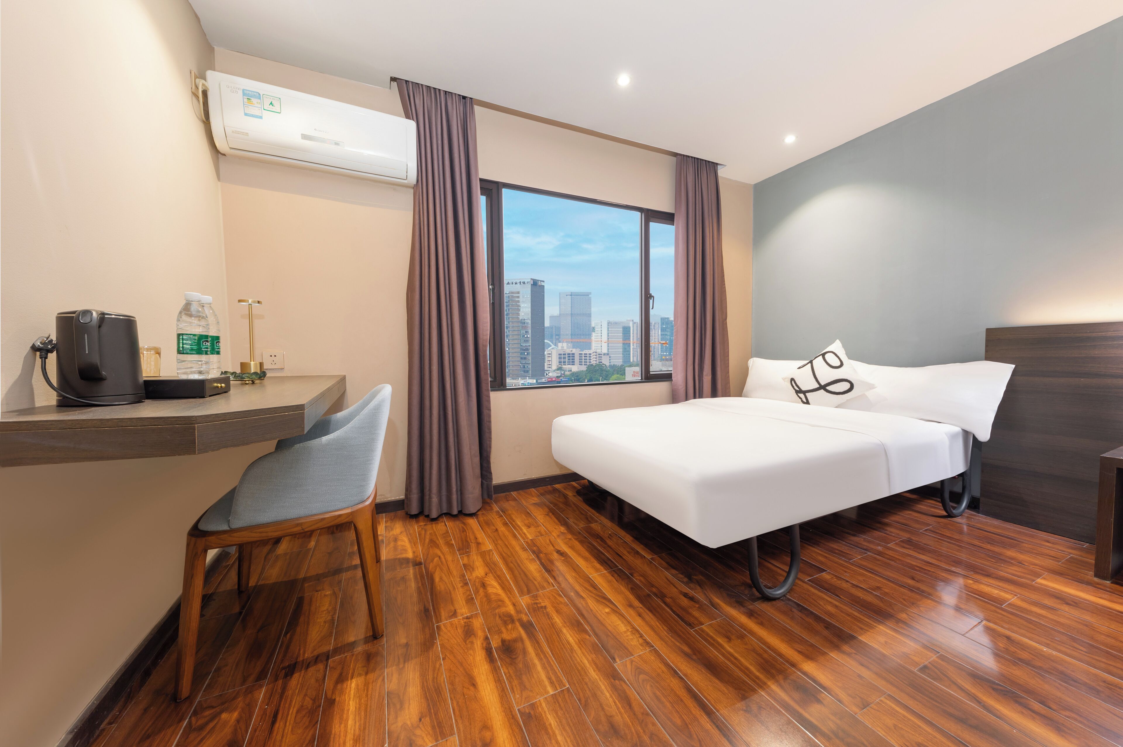 Una camera d'albergo con un letto, una scrivania con una sedia, una finestra con tende e vista sulla città.