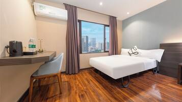 Una camera d'albergo con un letto, una scrivania con una sedia, una finestra con tende e vista sulla città.