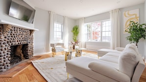 A modern living room with a stone fireplace, white sofas, a glass coffee table, and large windows with curtains. - Prime Luxury with Balcony Wood Fireplace (Yonkers)