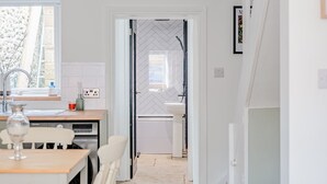 A modern kitchen with a window, a dining area with a table and chairs, and a hallway leading to a bathroom. - Cosy Cottage in Crewkerne, Free on Street Parking (Mudford)