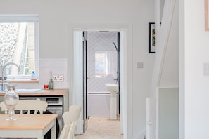 Une cuisine moderne avec une fenêtre, un coin repas comprenant une table et des chaises, et un couloir menant à une salle de bain.