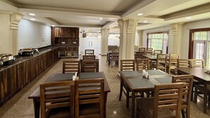 A spacious restaurant with wooden tables and chairs, a counter with a display, and a view of the street through large windows. - Hotel Alif Stay (Srinagar)