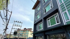 A multi-story building with a garage entrance, a parked car, and visible power lines. - Hotel Alif Stay (Srinagar)