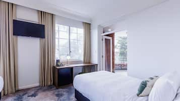A hotel room with a bed, a desk with a flat-screen TV, a window with curtains, and a view of the outside.