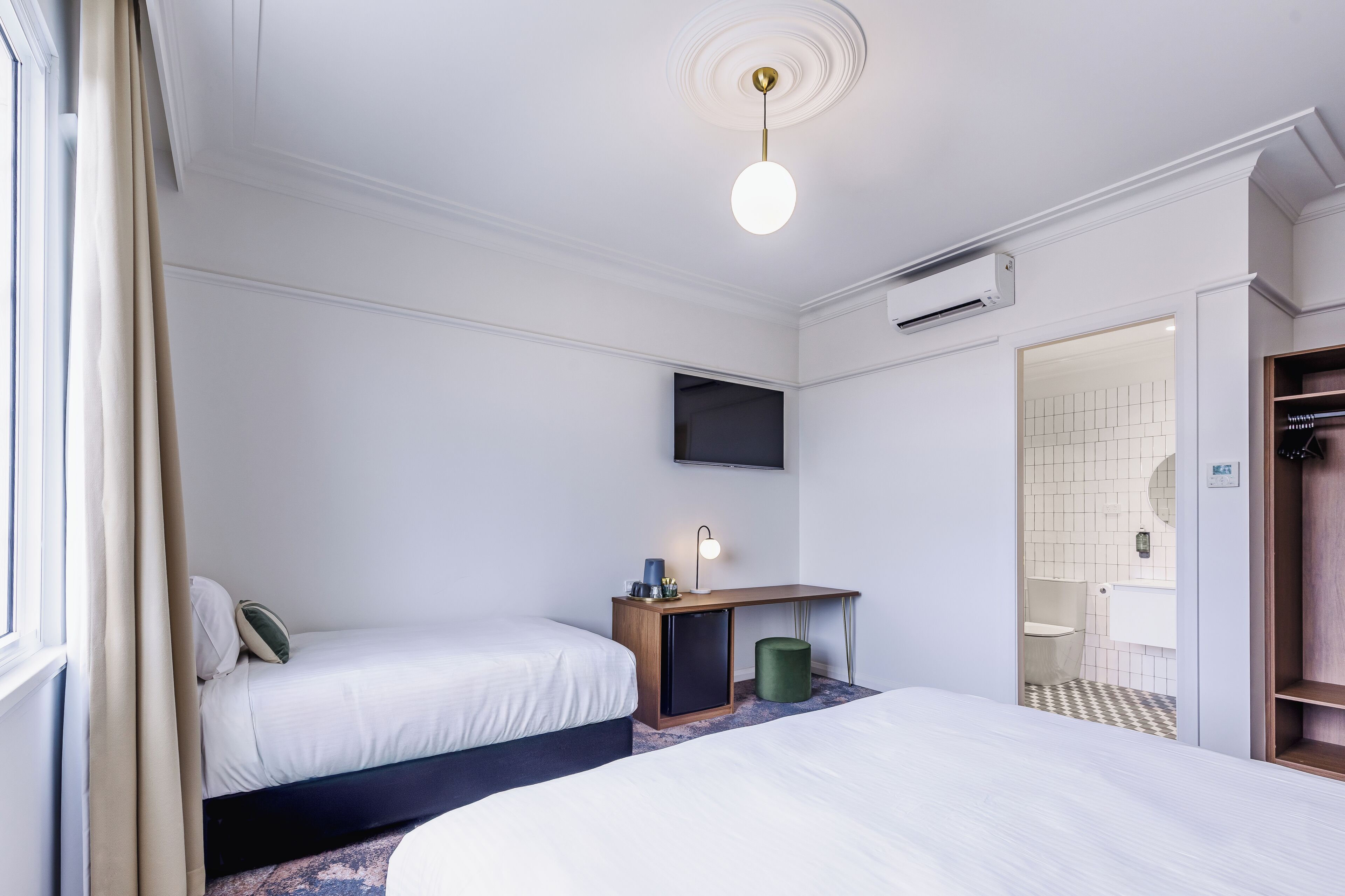 Ein Hotelzimmer mit zwei Betten, einem Schreibtisch mit Lampe, einem Fernseher und einem durch eine offene Tür einsehbaren Badezimmer.