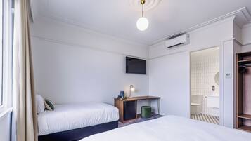 Ein Hotelzimmer mit zwei Betten, einem Schreibtisch mit Lampe, einem Fernseher und einem durch eine offene Tür einsehbaren Badezimmer.