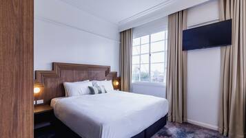 A hotel room with a large bed, a TV mounted on the wall, and a window with curtains.