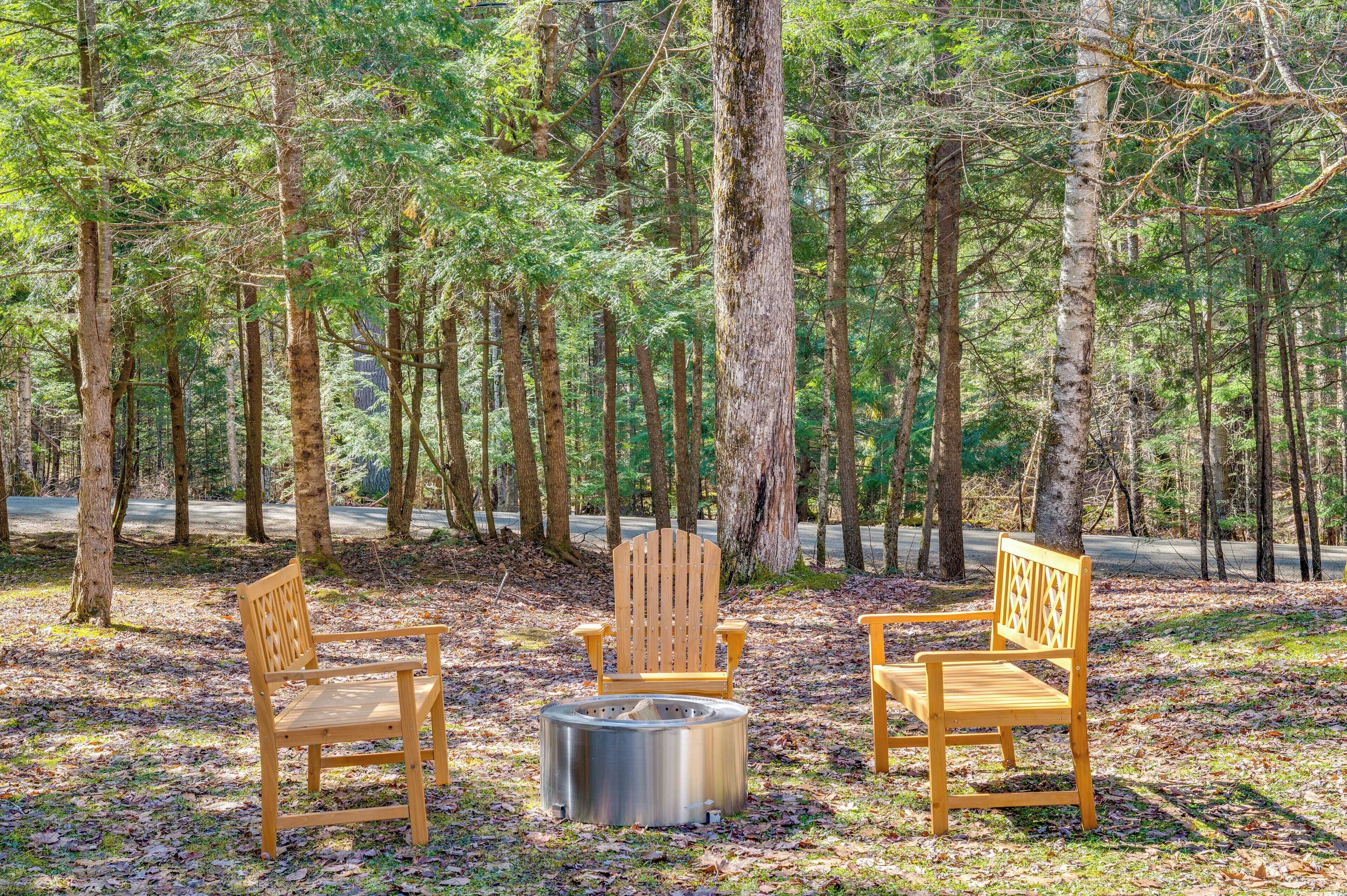 Zona boscosa con dos sillas Adirondack de madera y un brasero de metal.