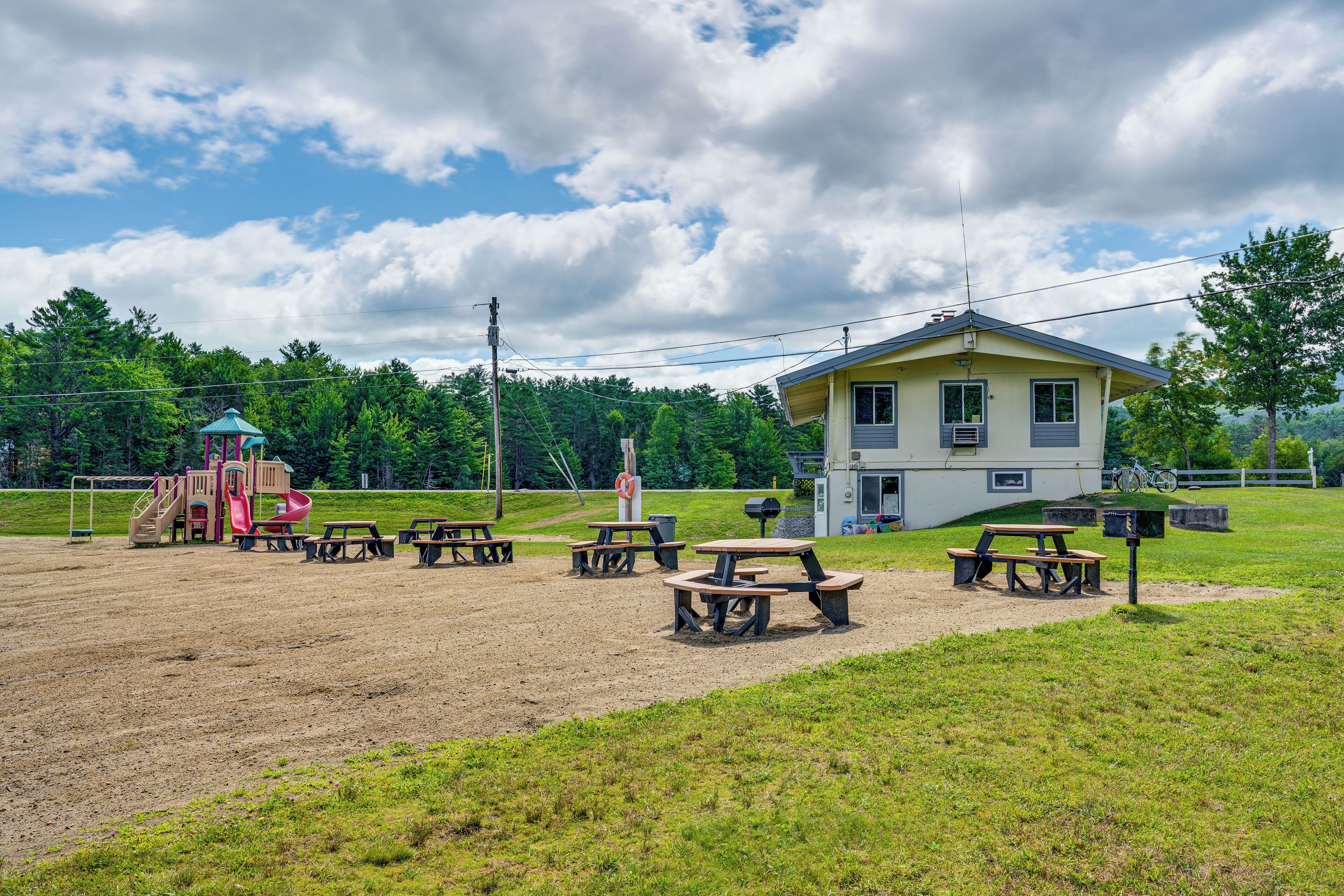 Ein Spielplatz mit Rutsche und Schaukeln, Picknicktischen und einem Haus im Hintergrund.