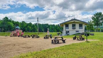 Ein Spielplatz mit Rutsche und Schaukeln, Picknicktischen und einem Haus im Hintergrund.