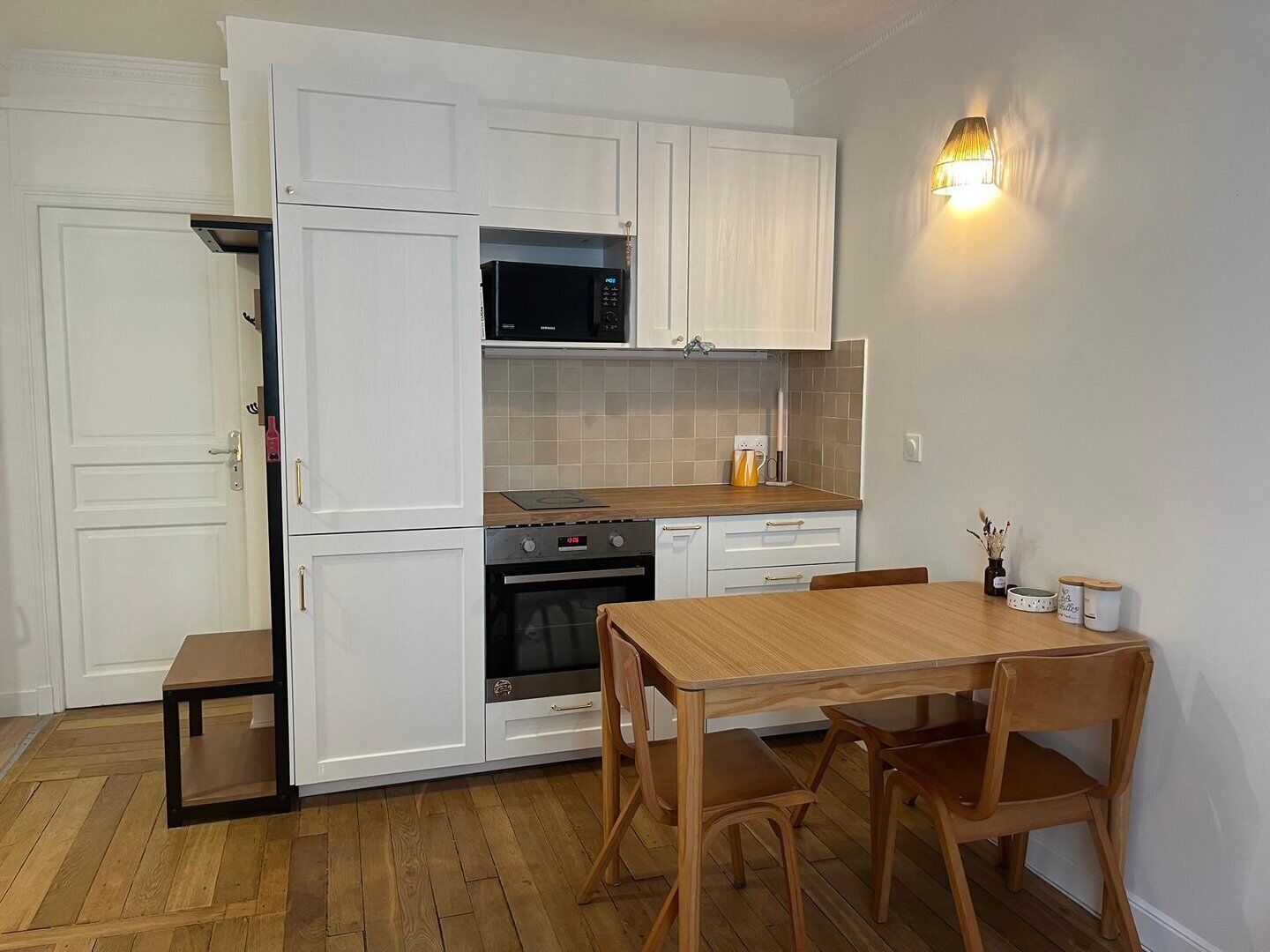 A compact kitchen with white cabinetry, a microwave, an oven, and a dining table with chairs.