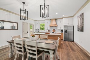 A modern kitchen with white cabinets, a stainless steel refrigerator, and a dining area with a wooden table and chairs. - Charming 3-bedroom house in brilliant Foley with AC, WiFi (Foley)