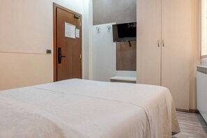 Un dormitorio con una cama, una puerta de madera, una pared blanca y un armario blanco.