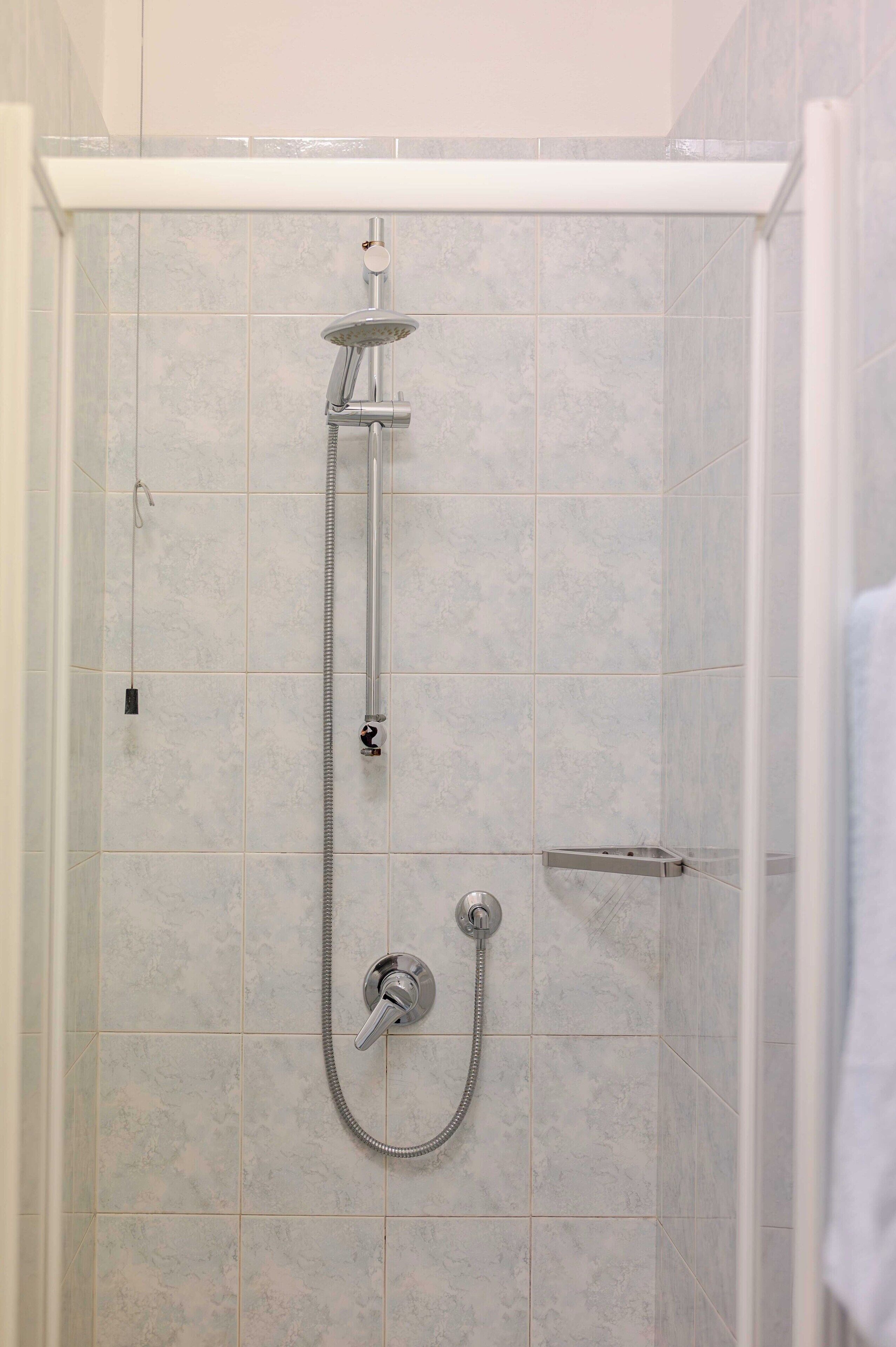 Una ducha a ras de suelo con cabezal de ducha de mano y otro fijo, paredes de azulejos y un organizador de ducha blanco.